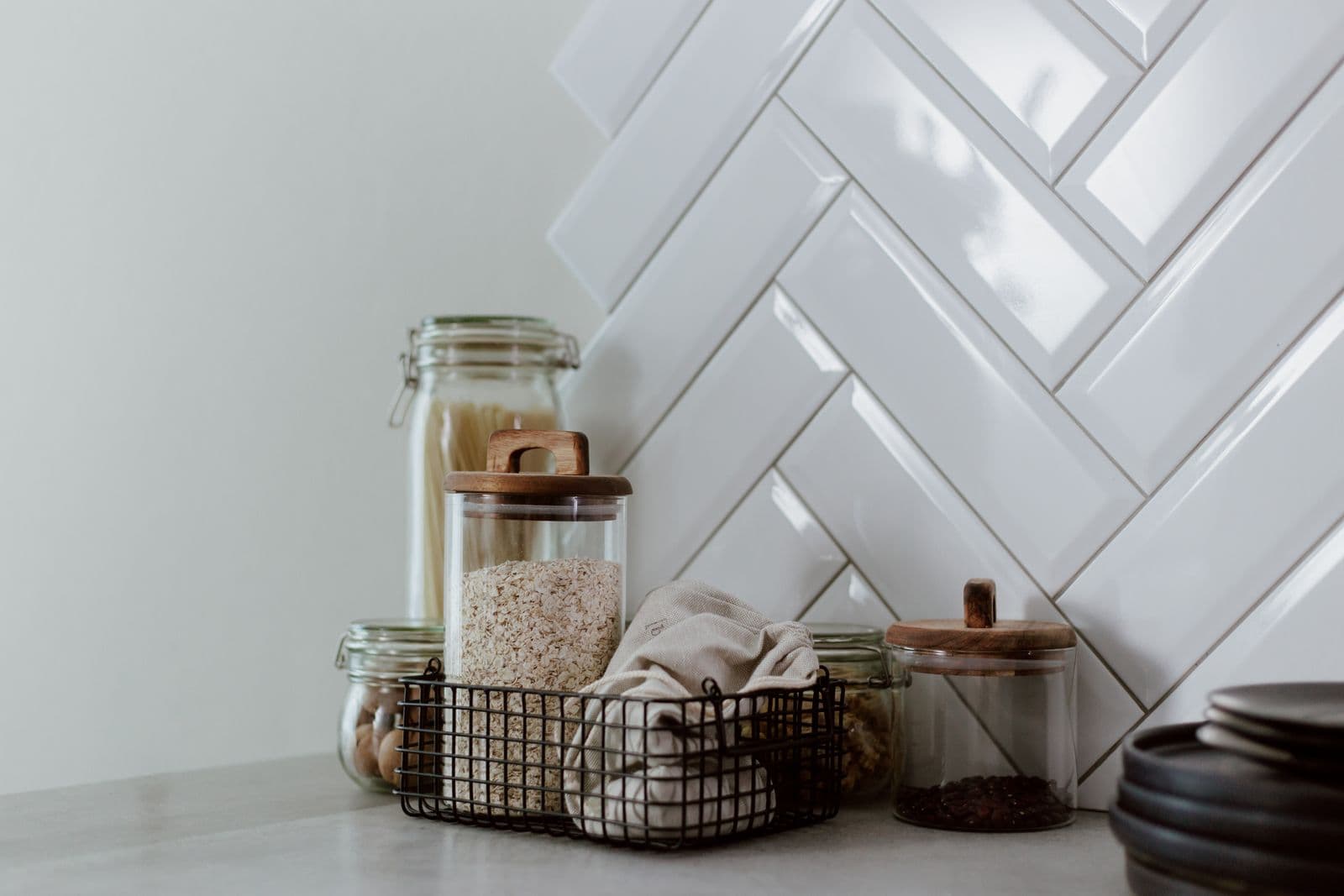 A tidy kitchen counter with storage jars against white herringbone tile